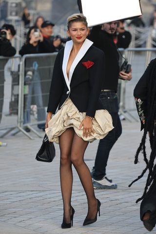 A photo of Zendaya wearing red lipstick, a sailor-inspired jacket, and a brown bubble skirt.