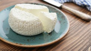 Wheel of ricotta sitting on plate next to knife