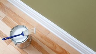 Pot of white paint on wooden floor next to white skirting board and green wall