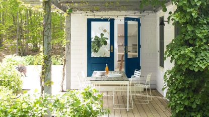An example of how to make a small garden look bigger with a covered decking area beside a white brick house with blue doors. 