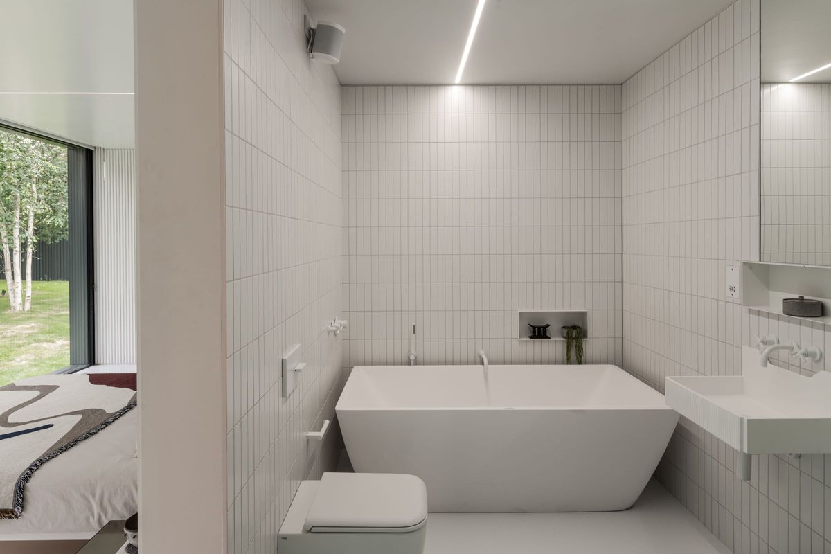 An en suite bathroom with white bath behind the wall behind the bed