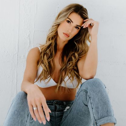 A portrait of Sydnee Falkner, sitting with one elbow balanced on her knee and resting her head on her hand.