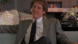 James Spader in a tan suit and a dark tie, sitting on a couch and smiling in White Palace