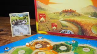 Catan box, board, cards, and pieces on a wooden table