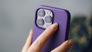 An iPhone in a purple case being held in a person's hand with the camera lenses visible