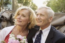 An older couple pauses just after remarrying. They are riding in a horse-drawn carriage and she is holding a bouquet.