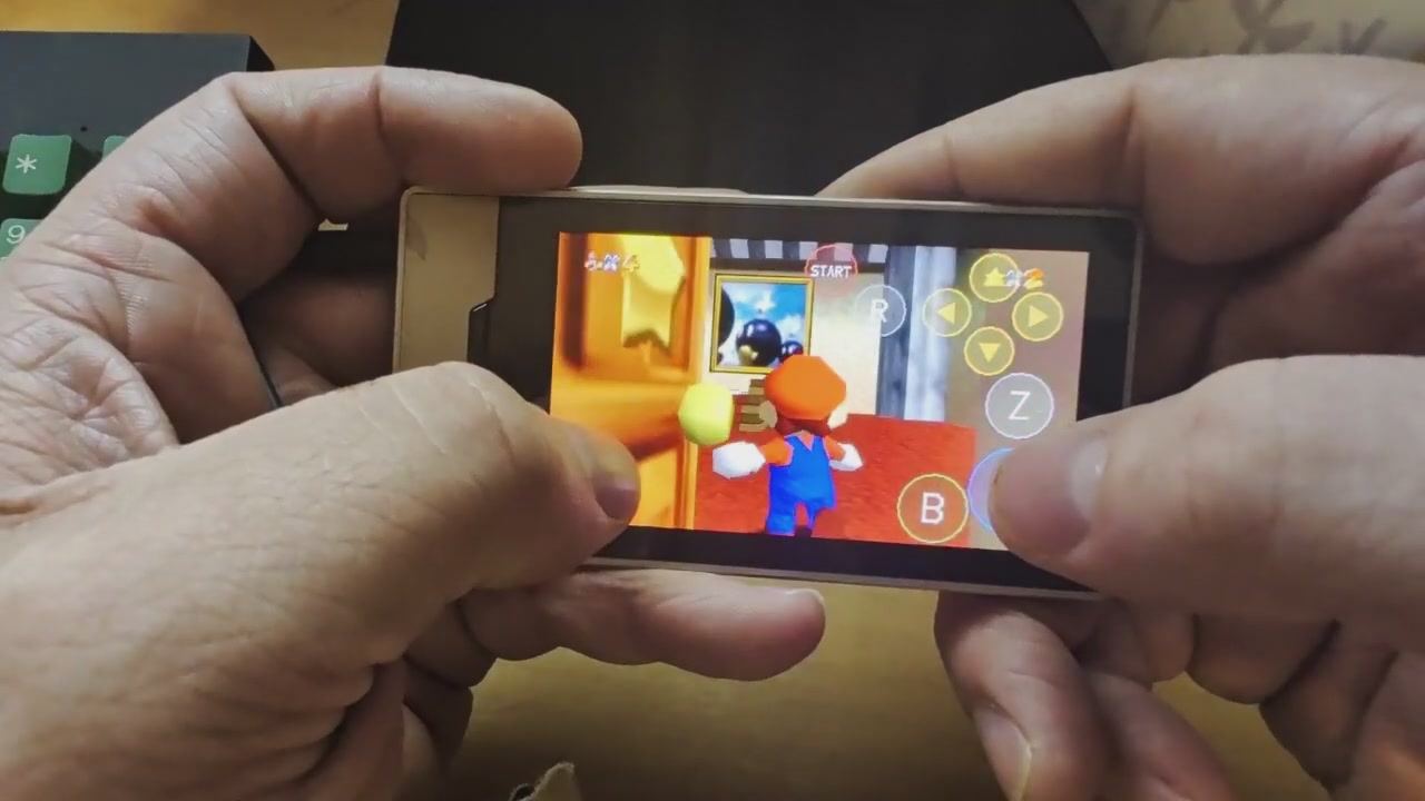 Hands holding a Zune HD sideways with Super Mario 64 running on its screen, Mario inside the castle and touch buttons overlaid on the right