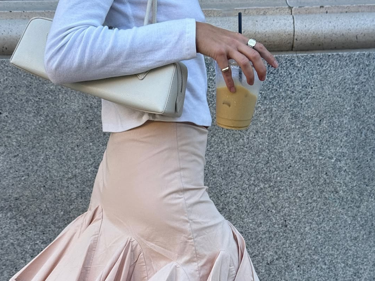 woman wearing pink skirt and white long sleeve t-shirt holding iced coffee