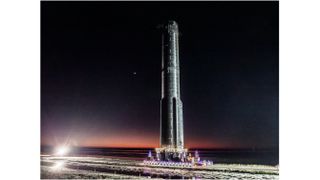 a large black rocket stands vertically against a dark sky.