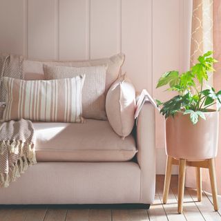 A pink living room with a pink sofa and matching cushions with the wall behind covered in wood panelling