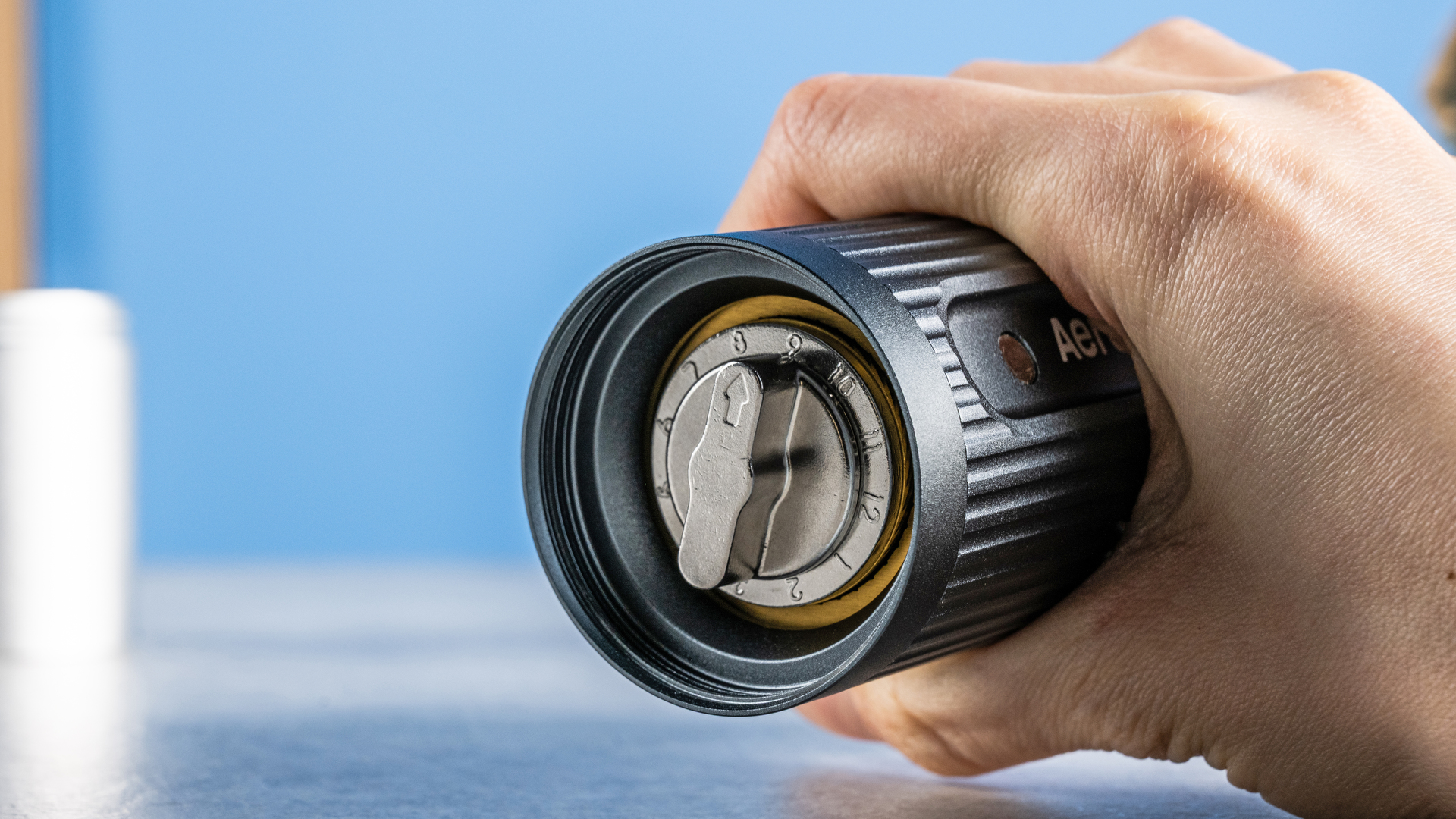 the aeropress manual coffee grinder in gray and silver against the tom's guide blue background