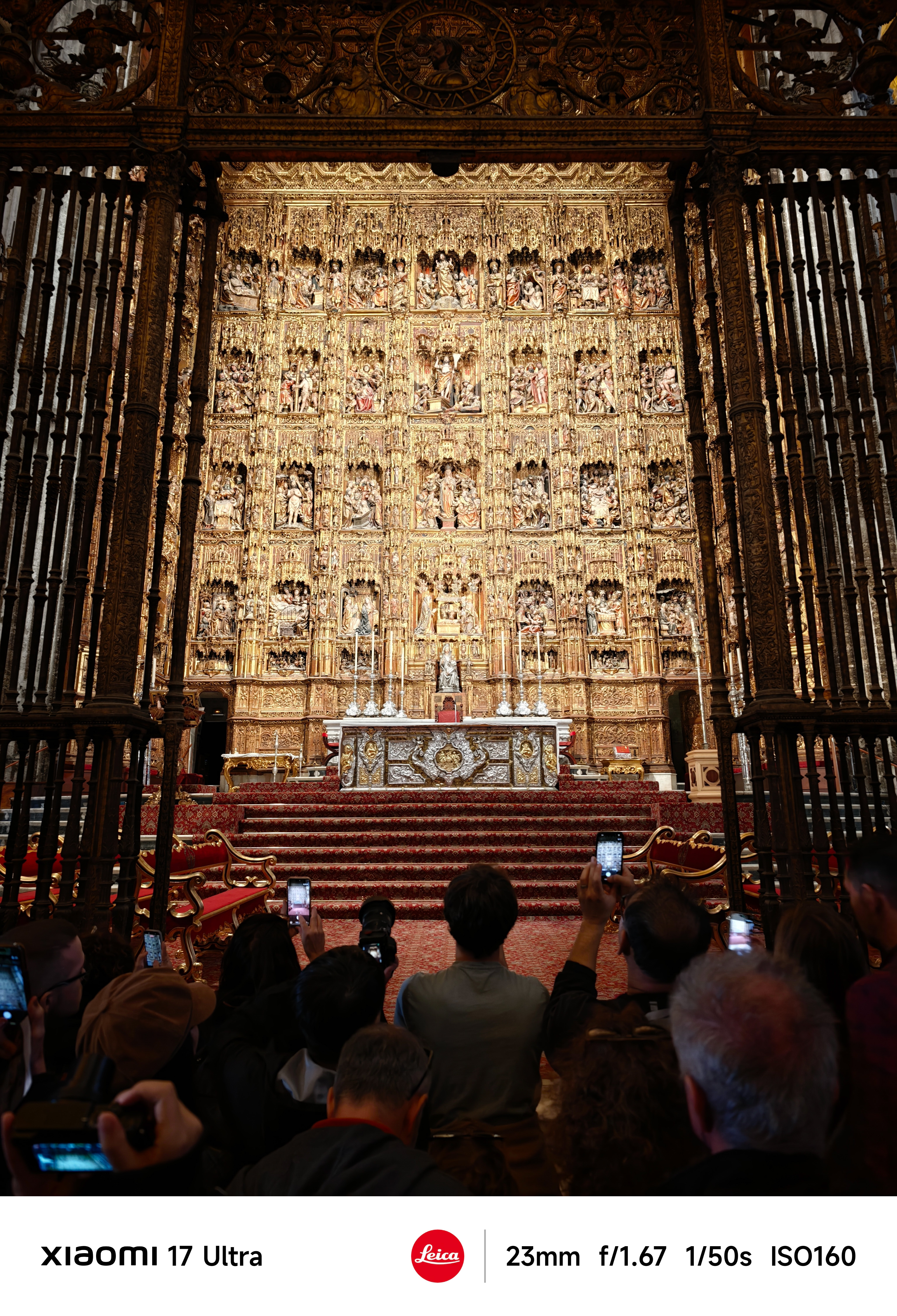 Ornate golden altarpiece inside a cathedral with visitors raising phones to take photos.