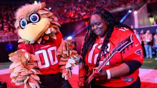 Diamond Rowe playing guitar next to a man dressed as a giant falcon