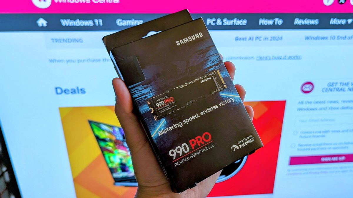 Samsung 990 PRO solid-state drive held in front of Windows Central deals page