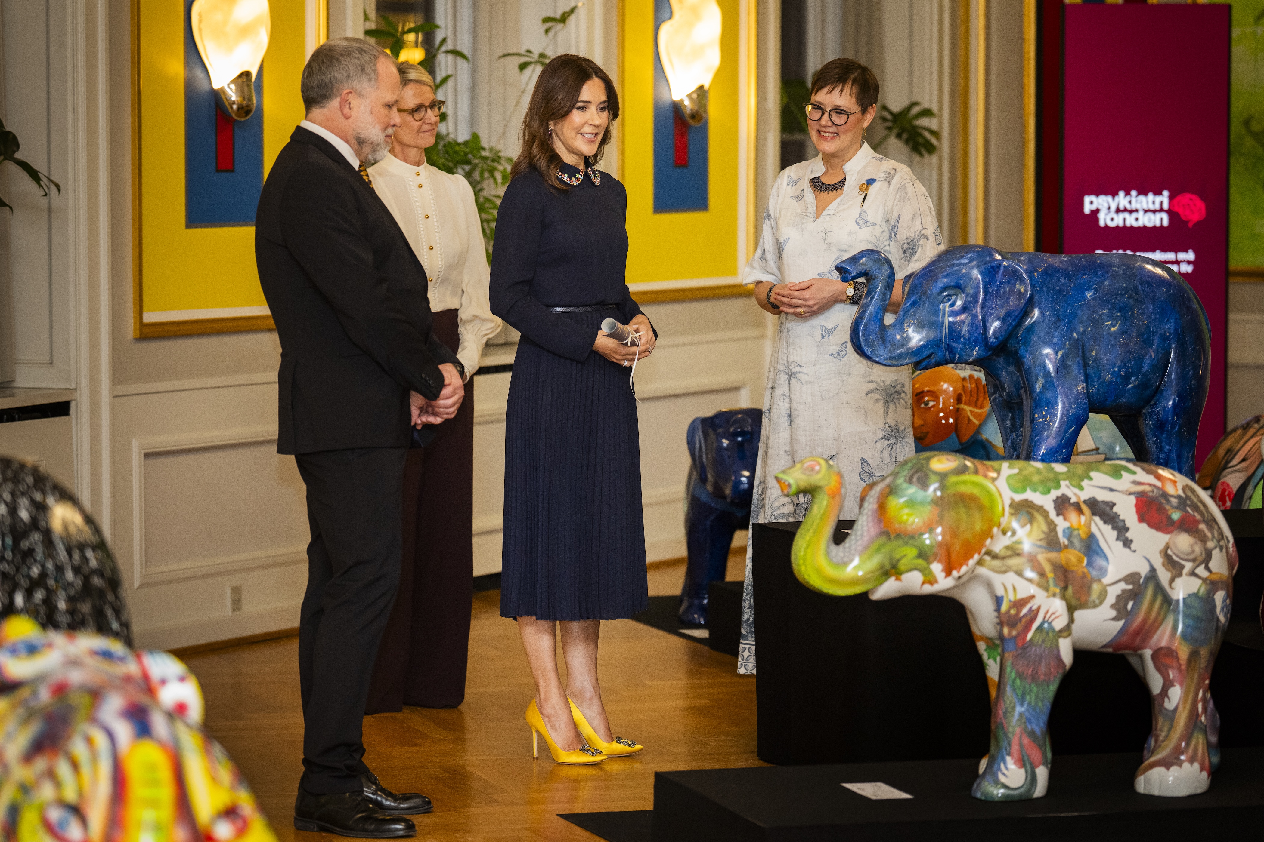 Queen Mary standing in a room in front of elephant statues