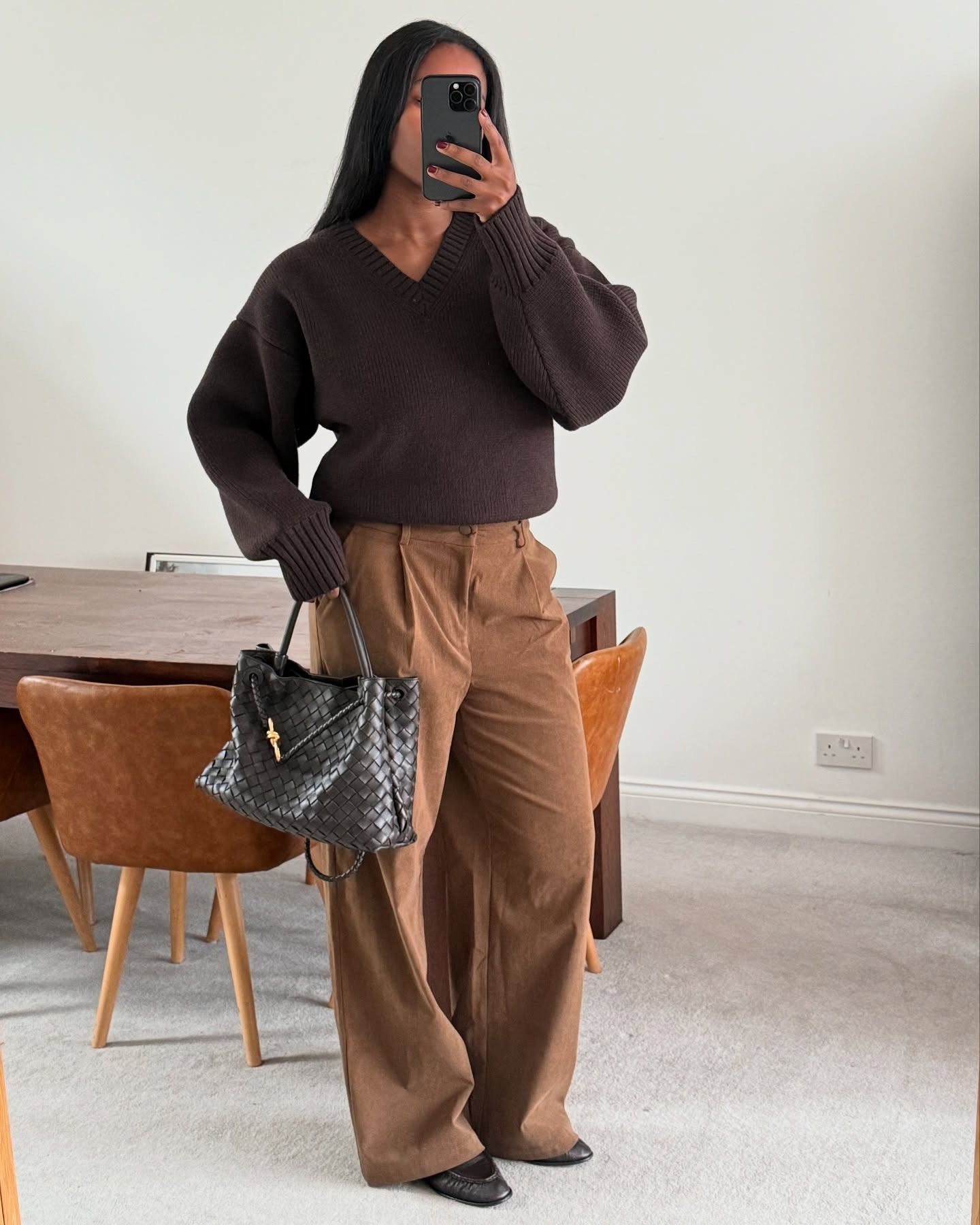 @nlmarilyn wearing a brown V-neck sweater, chestnut brown pants, black loafers, and a brown Bottega Veneta Andiamo bag.