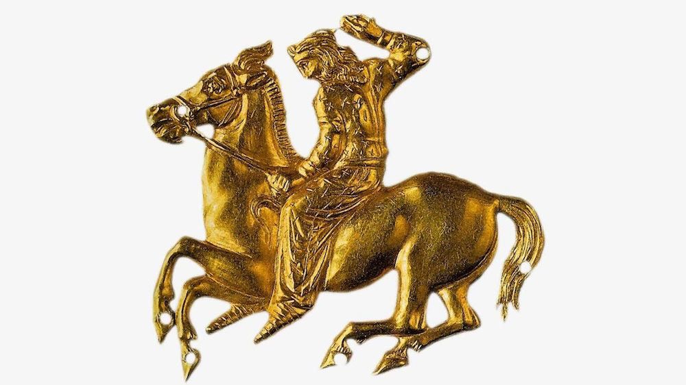 A gold Sythian artifact of a man riding on horseback.