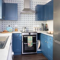 Blue kitchen with painted cabinets, chrome knobs, marble worktop, geometric tiles, wooden floor