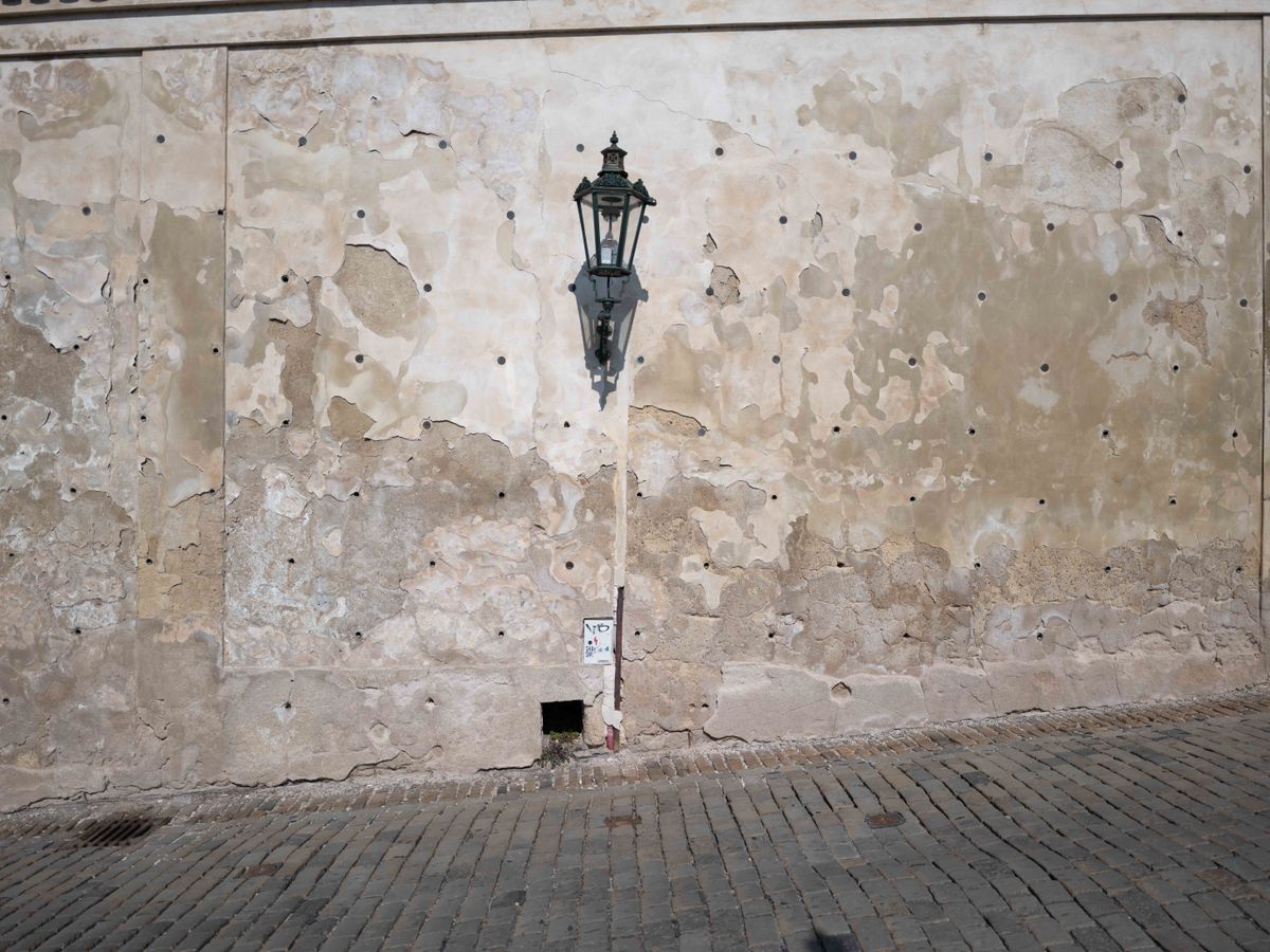 Flaking stone wall in a cobbled street with a single street lamp