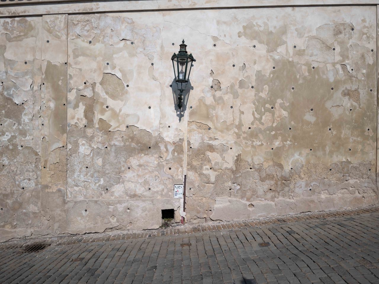 Flaking stone wall in a cobbled street with a single street lamp
