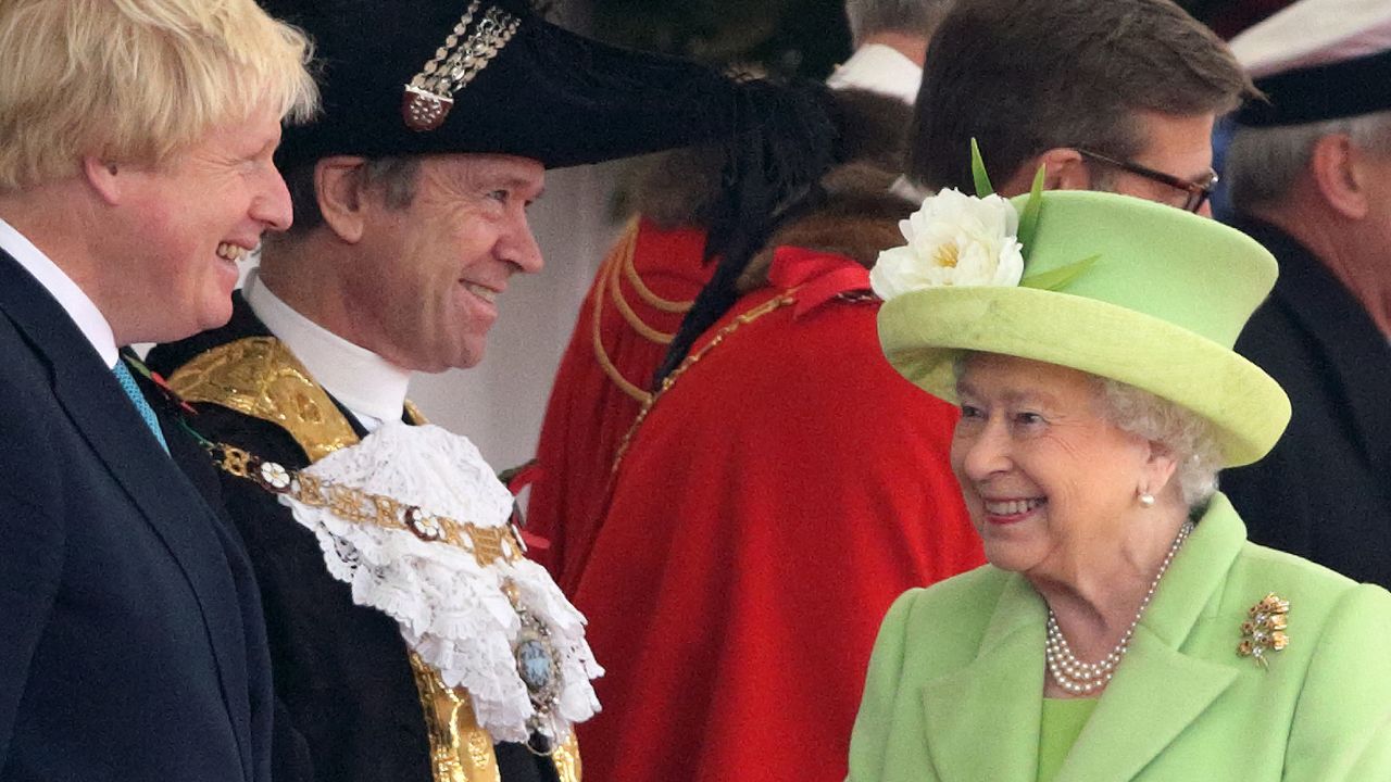 Queen Elizabeth smiling in a green coat while talking to Boris Johnson