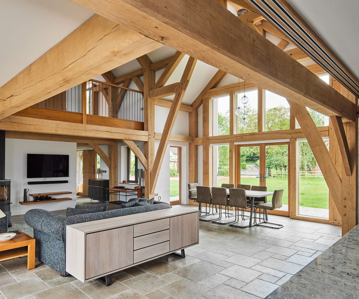 A living area in an oak frame home with double-hight ceilings. The floors are natural stone and there are plenty of exposed oak beams