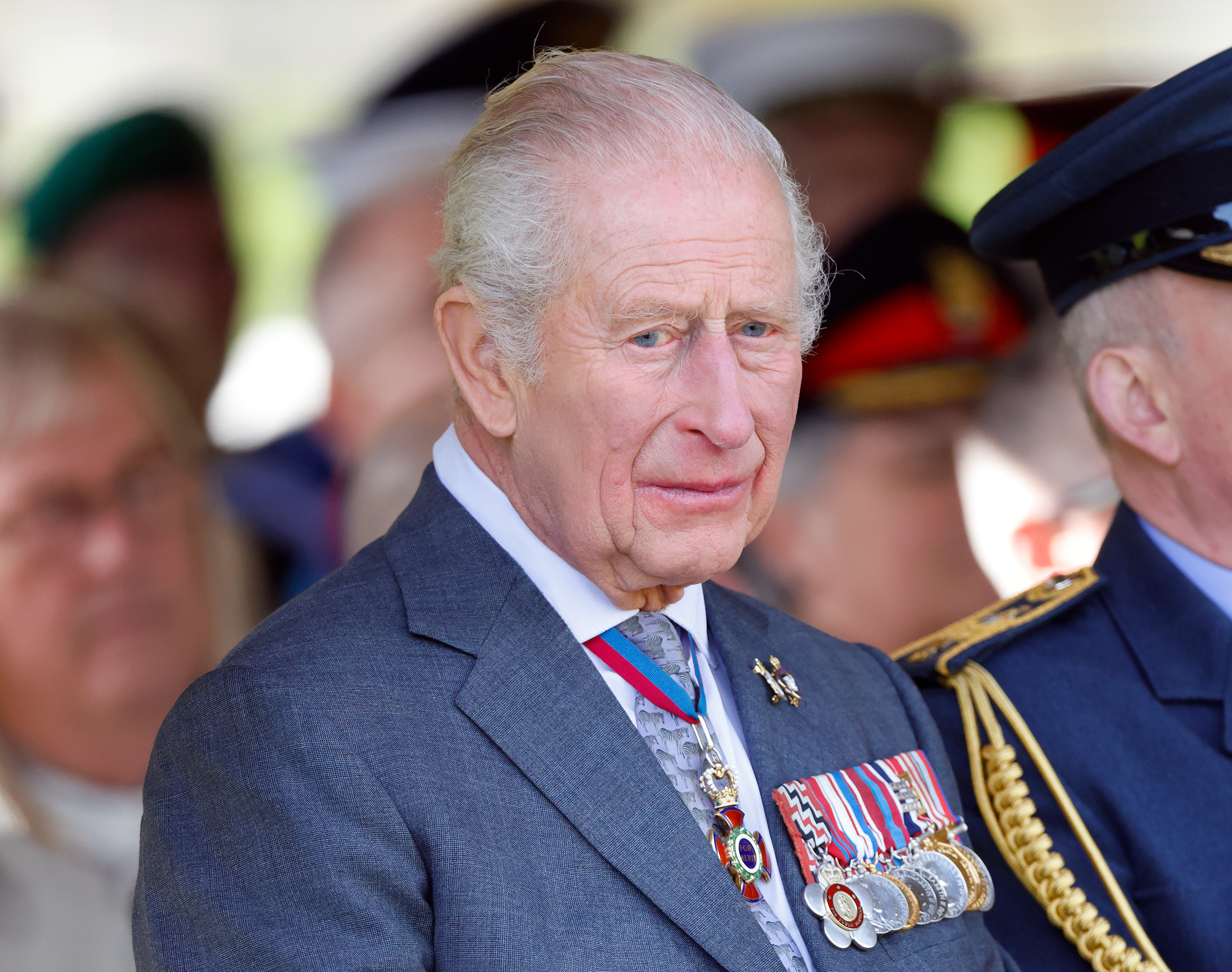 King Charles wearing a suit with medals and looking downcast
