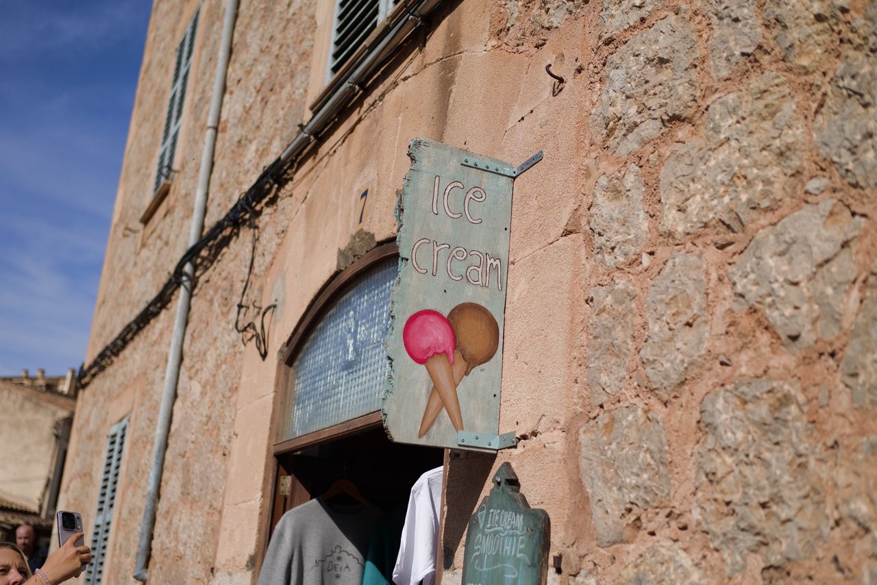 Rustic hand-painted ice cream sign mounted on a stone building in bright sunlight.