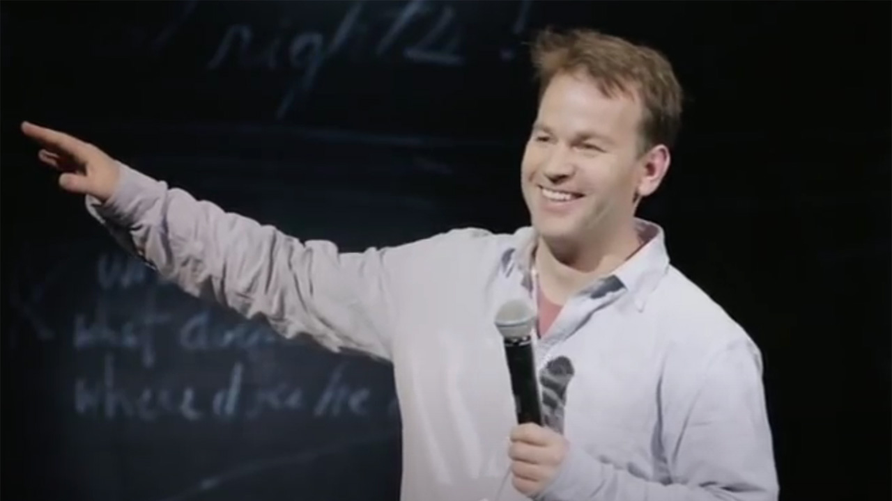 Mike Birbiglia pointing to the side of the stage in My Girlfriend's Boyfriend on Netflix.