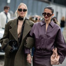 two fashion week attendees wearing sunglasses and green and dark red coats