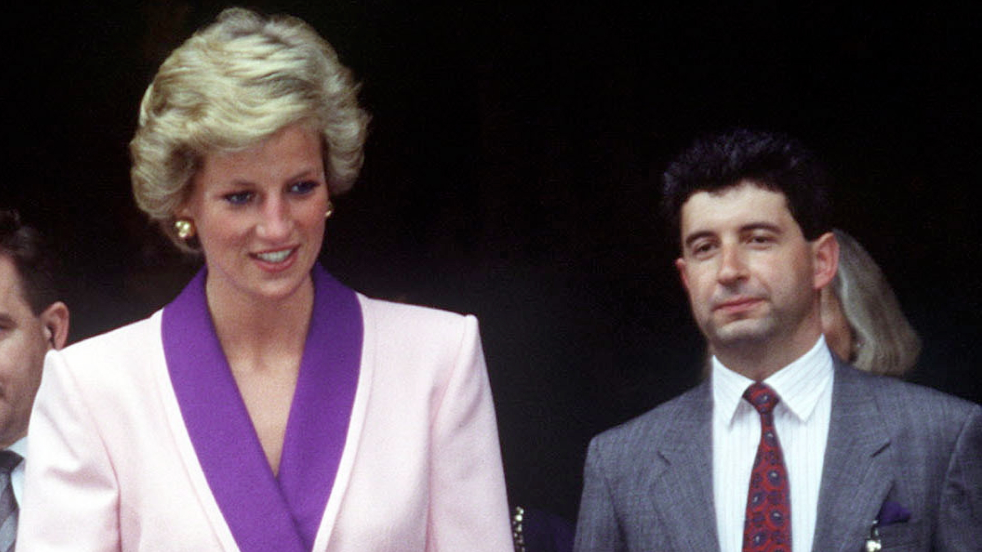 Princess Diana in Budapest, Hungary wearing a pink coat dress with purple accents, and her Private Secretary Patrick Jephson walking behind her 