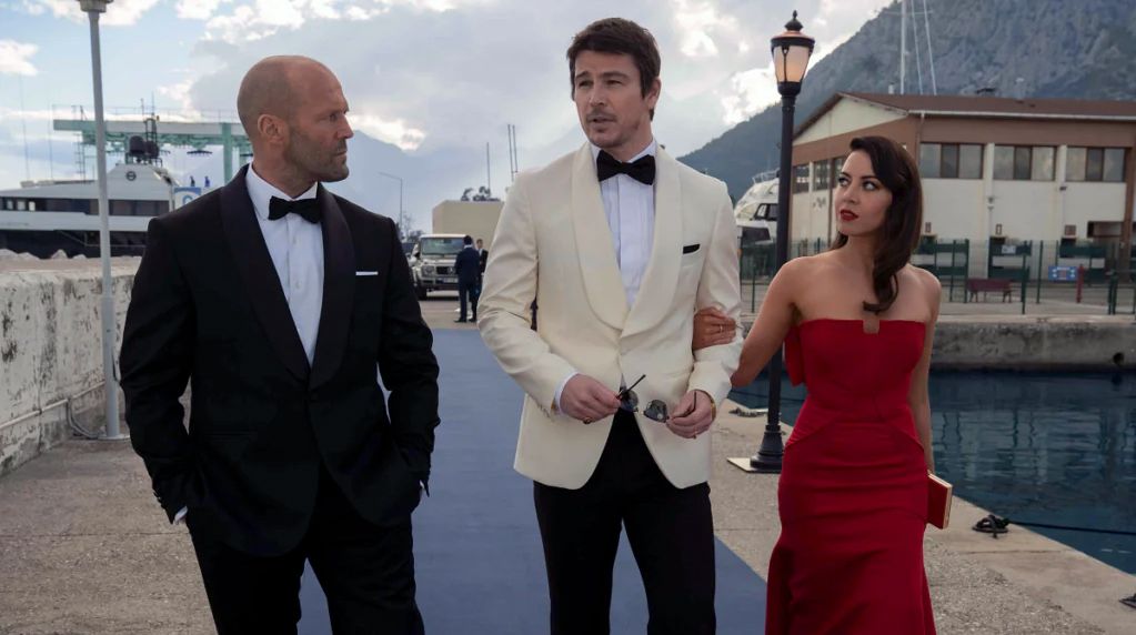 (L to R) Jason Statham as Orson Fortune, Josh Hartnett as Danny Francesco, and Aubrey Plaza as Sarah Fidel in formal attire, walking on a pier in Operation Fortune: Ruse de Guerre