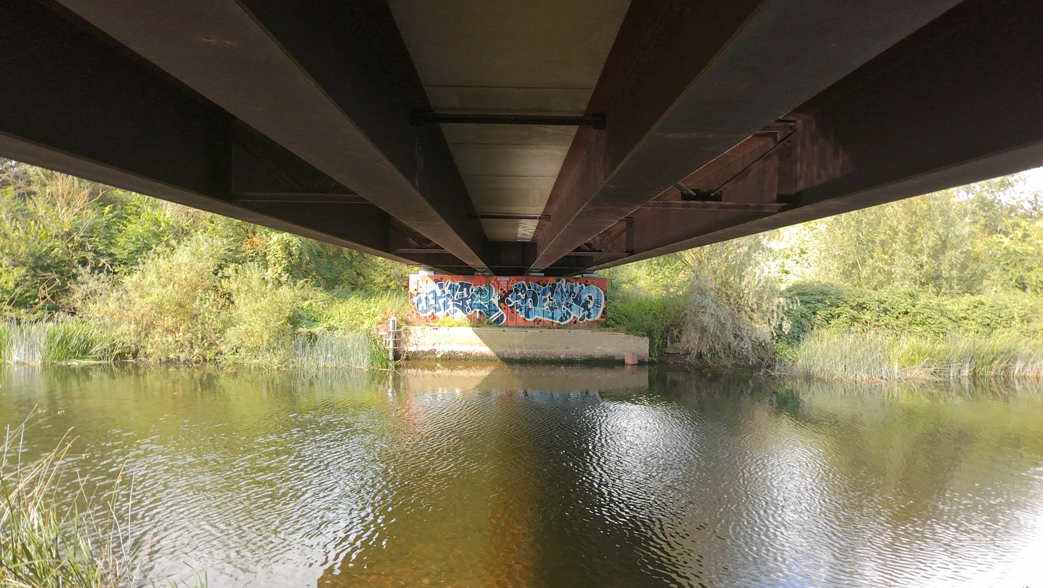 View of the underside of a bridge over a river with graffiti taken by DJI Neo.