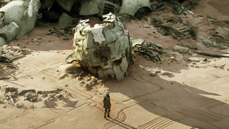 A weathered robot head lies in the sand.