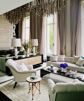 white living room with cream sofa and armchairs, cream rug, black coffee table and brass chandelier