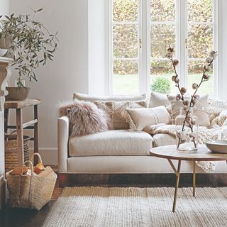 A living room with a large window and cream sofa with textured scatter cushions and a matching rug with a round coffee table on top