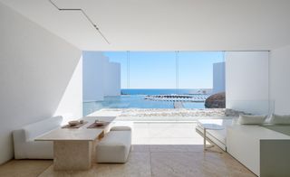 Sunroom overlooks pools and ocean through glass wall with bed, couches and table