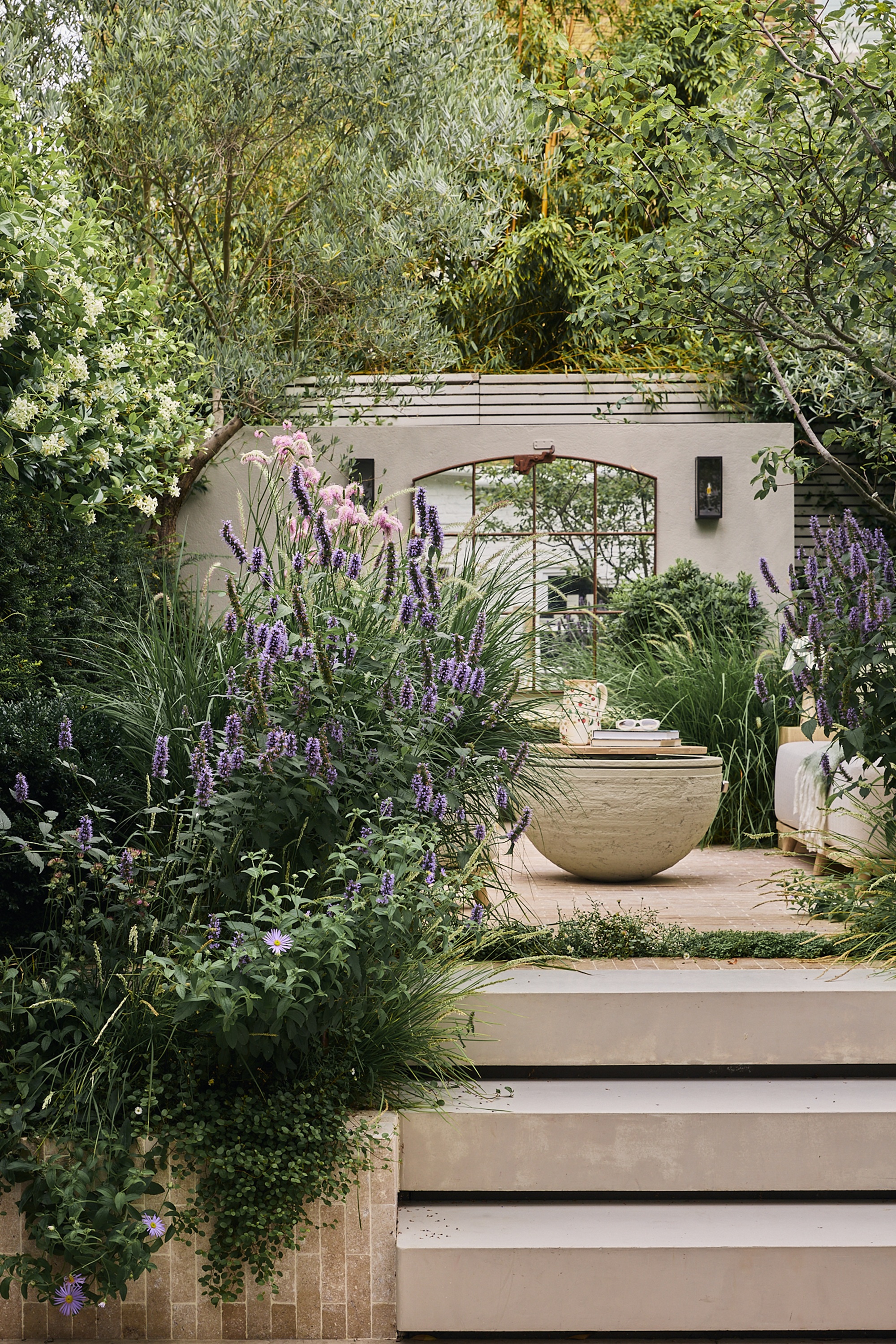 a modern garden with lush planting, purple flowers, and sculptural landscaping