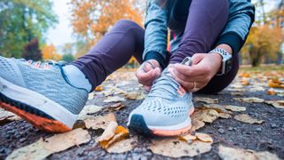 woman sat on a leafy pavement lacing up her running shoes