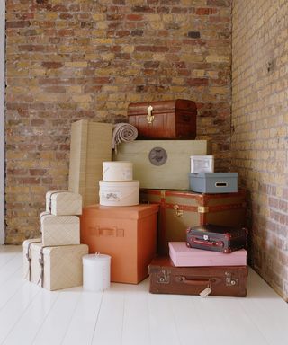 Suitcases and hat boxed piled up by a brick wall