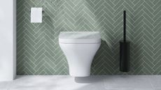 A white toilet mounted on a bathroom wall with mint green tiles and black toilet brush and holder