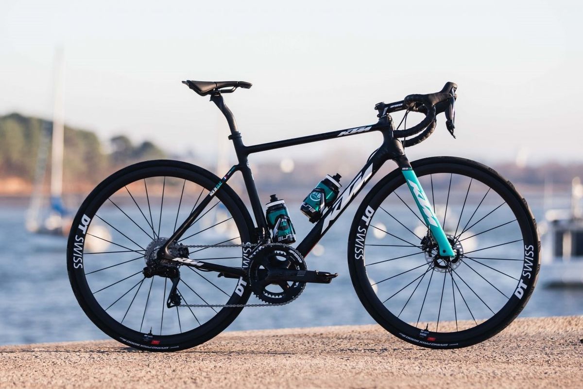 A road bike stands in front of the water with yachts behind