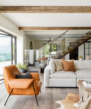 living room with neutral walls, wooden beam ceilings, white sofa and orange armchair