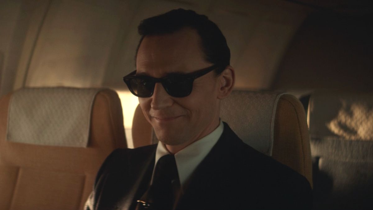 Tom HIddleston smiles while sharply dressed on a plane in Loki Season 1.