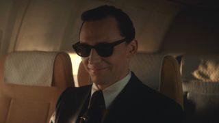 Tom HIddleston smiles while sharply dressed on a plane in Loki Season 1.