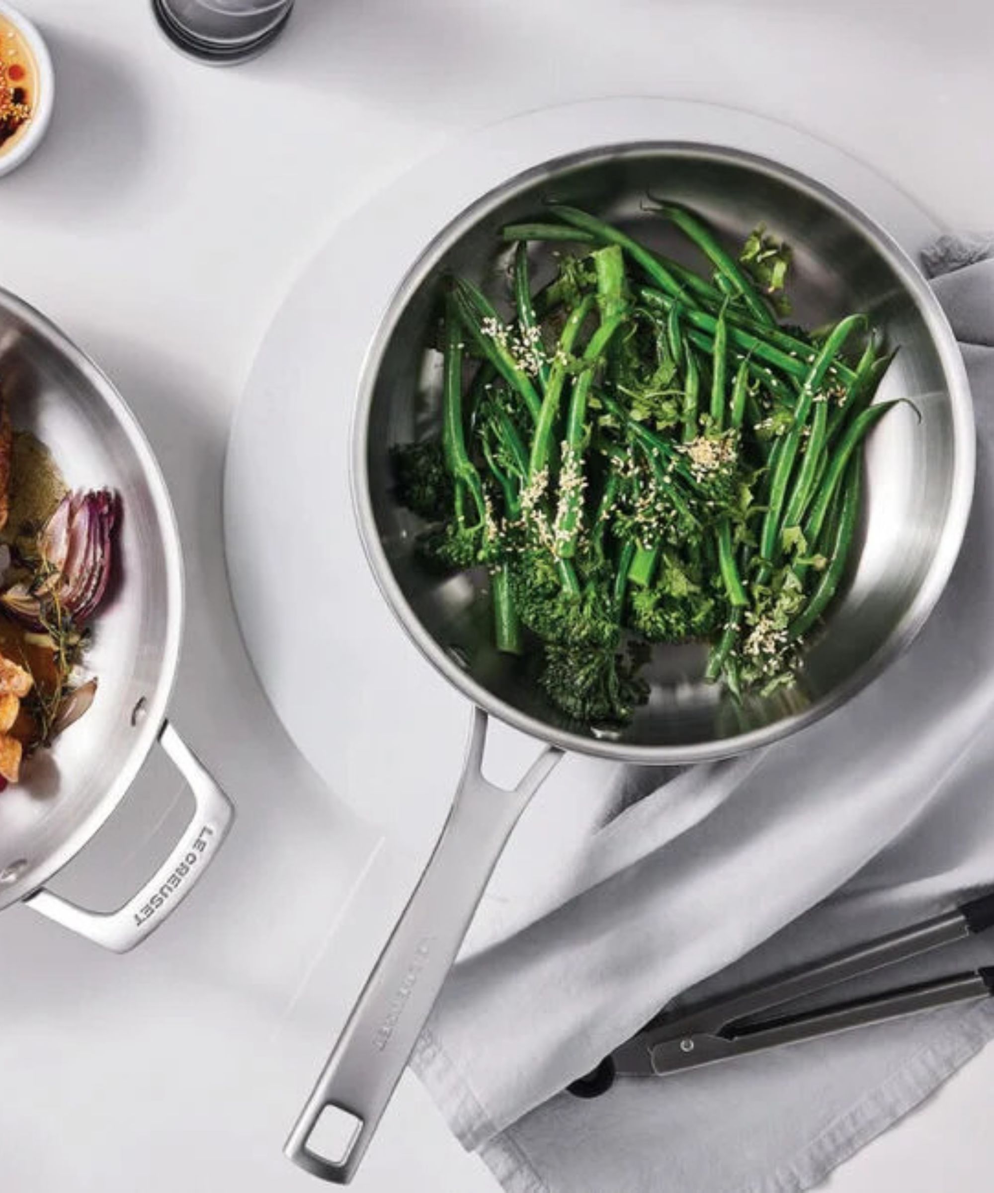A small stainless steel frying pan with fried broccoli inside, on a white table