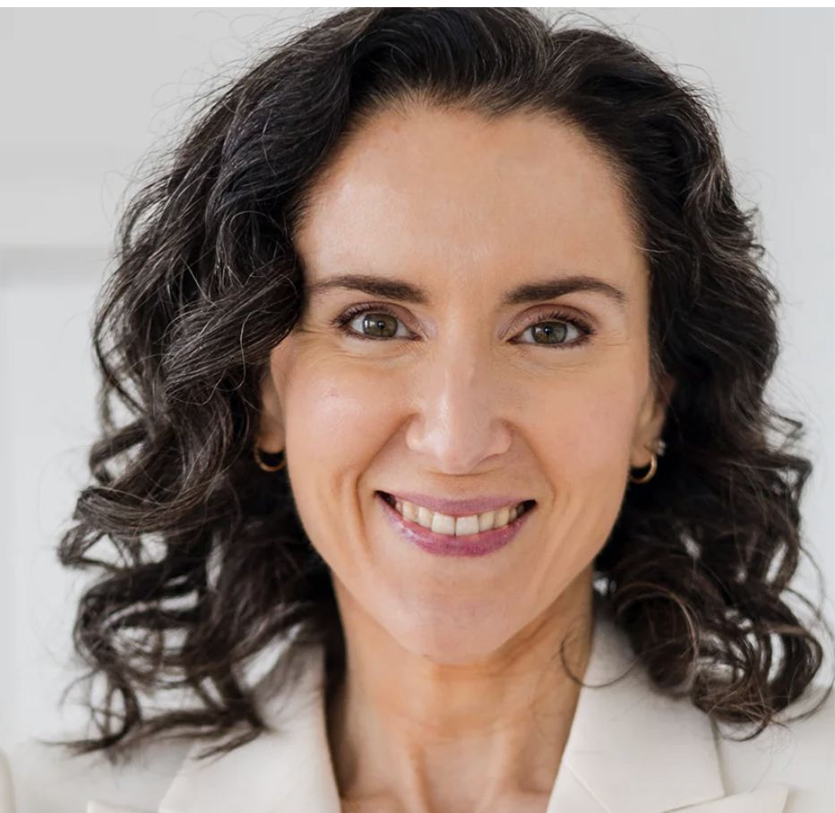 a white woman with dark curly hair in a white suit jacket