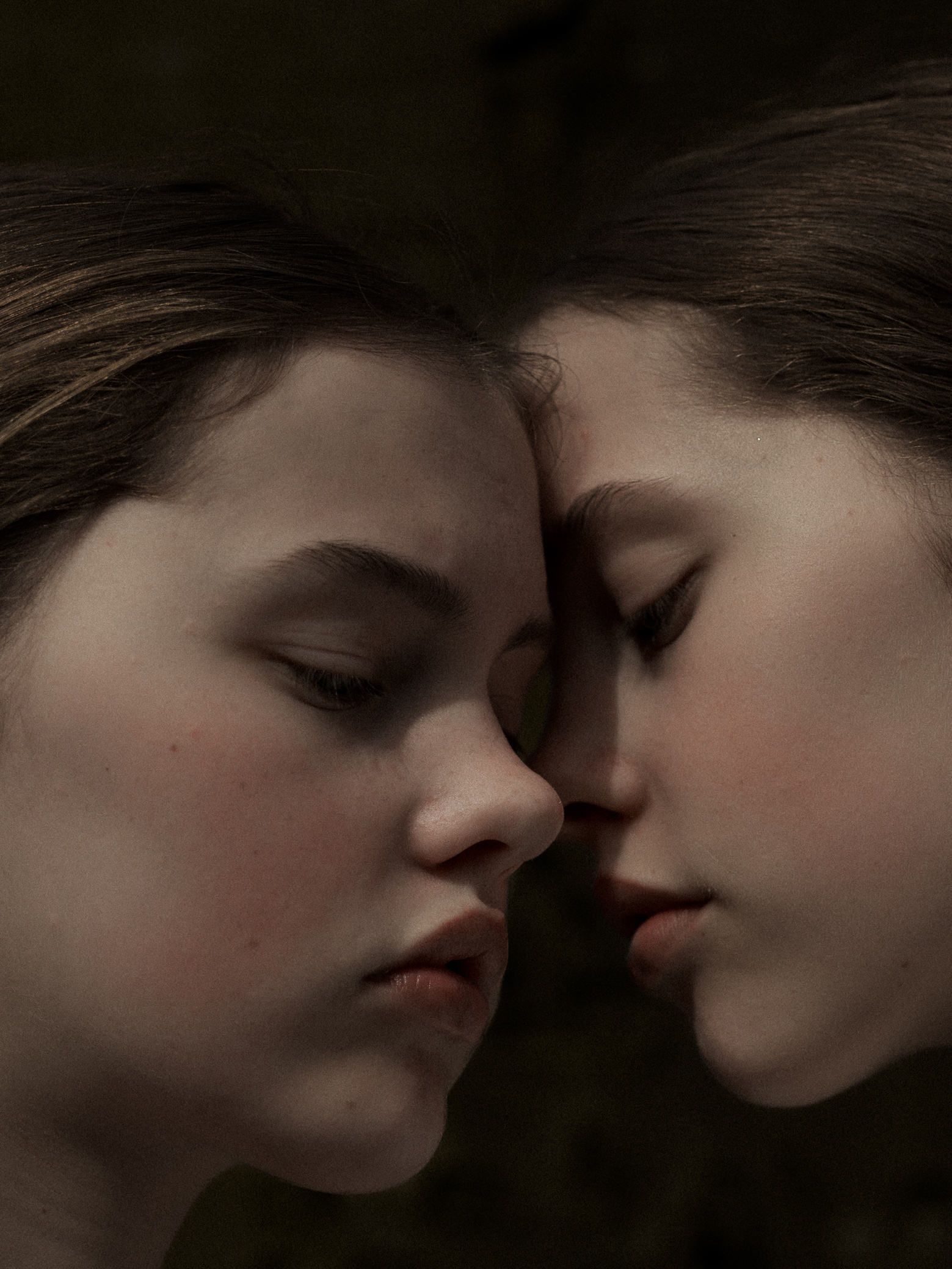 Close-up of two young women with foreheads touching, eyes closed in a tender, intimate moment