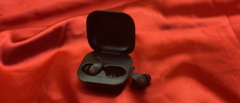 The Beats Fit Pro true wireless earbuds in their charging case on a red backdrop next to an Apple Watch