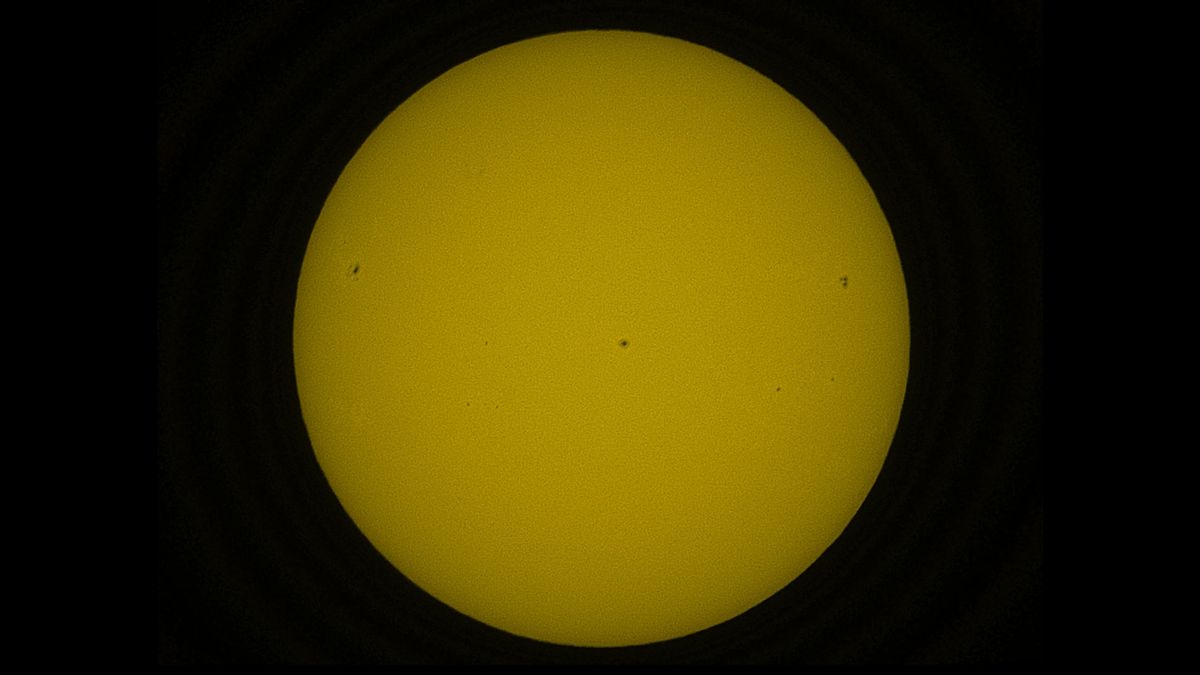 The solar disk in orange, showing dark sunspots.